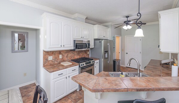 A kitchen with white cabinets, a stainless steel refrigerator, a microwave, and a gas stove.