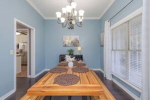 A dining room with a wooden table, decorative placemats, a chandelier, and a window with blinds.