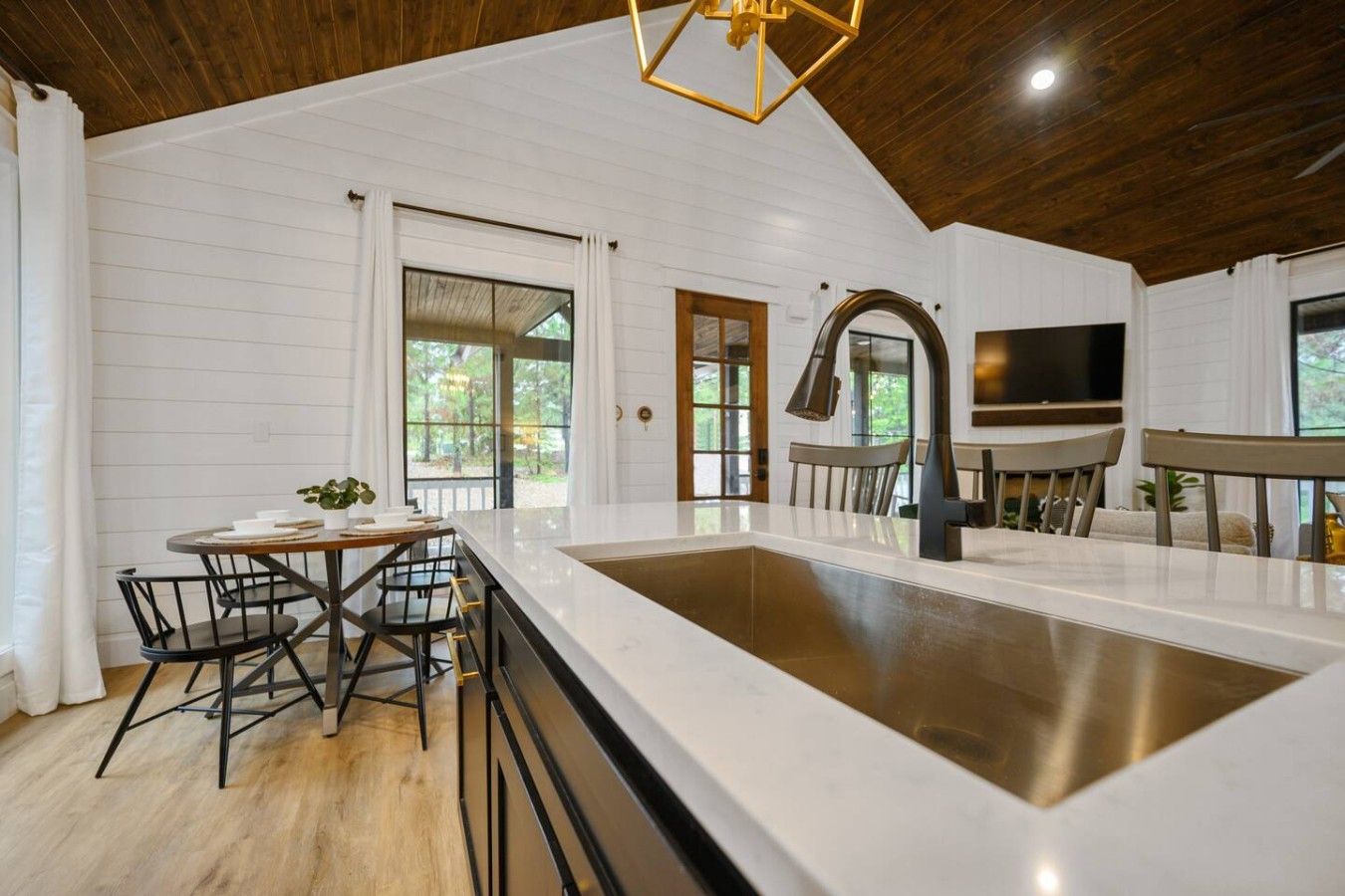 A modern kitchen with a large island, wooden ceiling, and a dining area with chairs and a table.