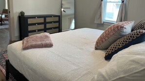 Een slaapkamer met een bed, een dressoir, een spiegel en een raam met gordijnen.