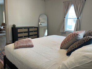 Un dormitorio con cama, cómoda, espejo y ventana con cortinas.