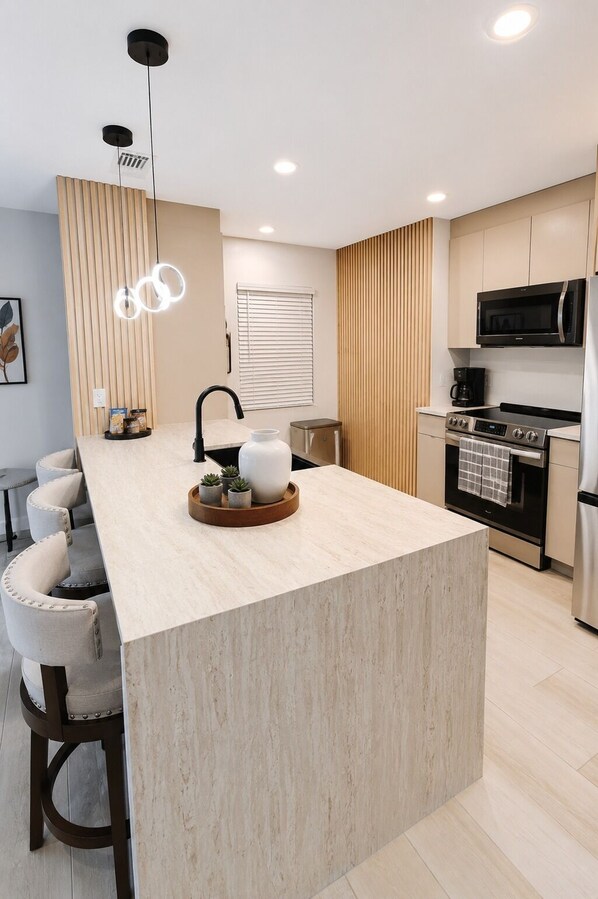 Cozinha moderna com ilha central, eletrodomésticos embutidos e luminária pendente.
