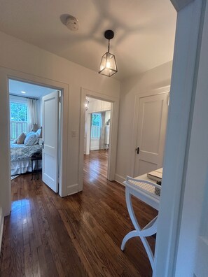 A hallway with wooden flooring, white doors, and a hanging light fixture.