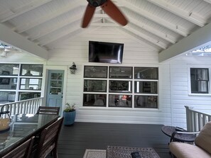 Eine überdachte Veranda mit Esstisch und Stühlen, einem Deckenventilator und einem großen Fenster mit vielen Glasscheiben.