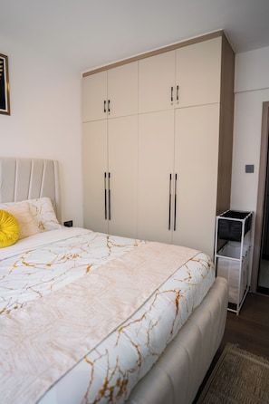 A bedroom with a bed, a wardrobe, and a small storage unit. - Modern 1BR at Golden Mango Heights  Gym, Sauna, Washer & Dryer (Nairobi)