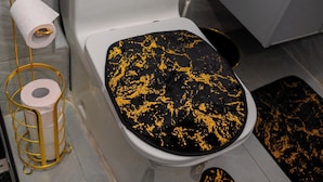 Ein Badezimmer mit Toilette, einer Toilettenpapierrolle und einer schwarzen Matte mit Gold-Spritzdesign auf dem Boden.