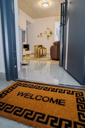 Een modern interieur met een marmeren vloer, een welkomstmat, een bank en een eethoek met een tafel en stoelen in goudkleur.
