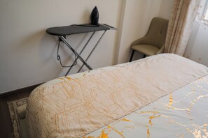 A neatly made bed with a patterned bedspread, a small ironing board, and a chair against the wall. - Modern 1BR at Golden Mango Heights  Gym, Sauna, Washer & Dryer (Nairobi)