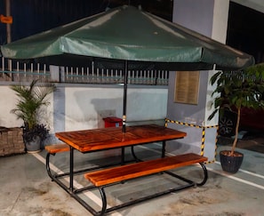 A wooden picnic table with a green umbrella, surrounded by potted plants and a metal fence. - Modern 1BR at Golden Mango Heights  Gym, Sauna, Washer & Dryer (Nairobi)
