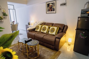 A modern living room with a brown leather sofa, a small round table, and a refrigerator. - Modern 1BR at Golden Mango Heights  Gym, Sauna, Washer & Dryer (Nairobi)