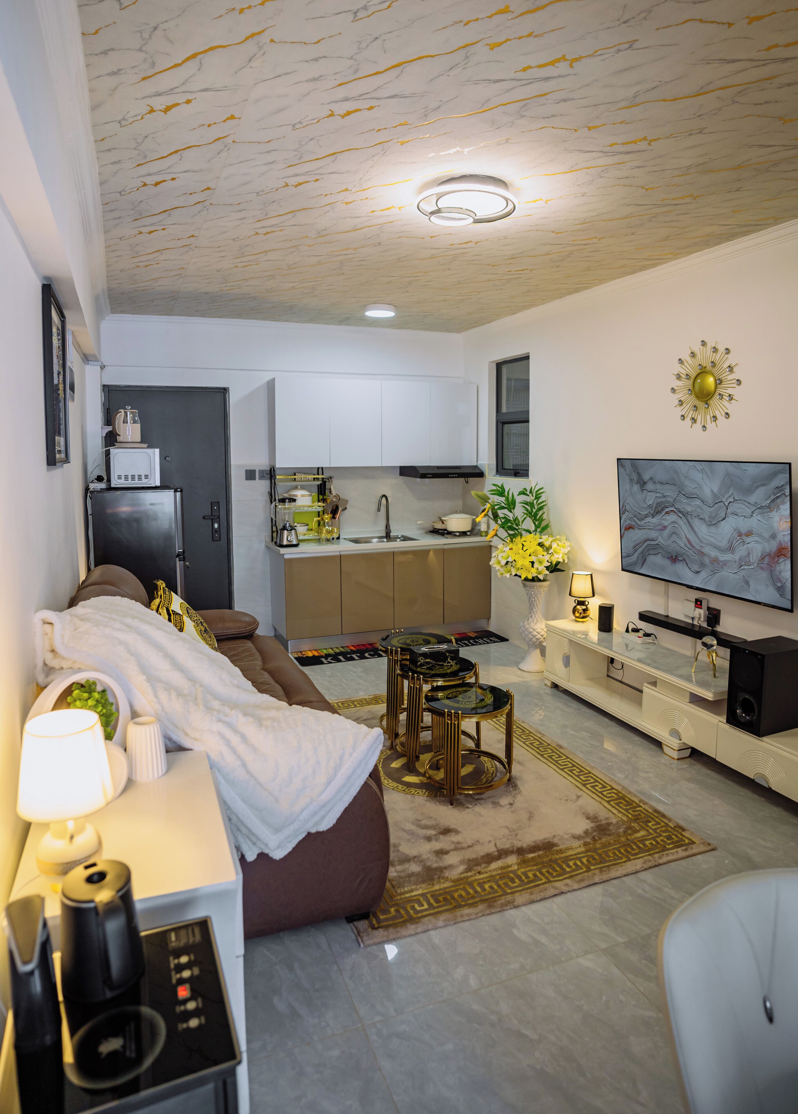 A modern living room with a sofa, coffee table, TV, and kitchen in the background.