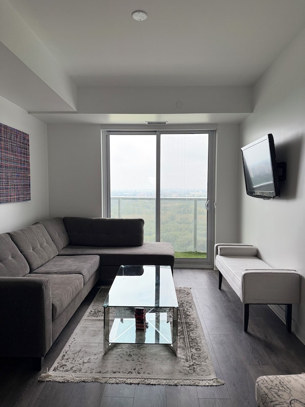 A modern living room with a grey sofa, a glass coffee table, and a TV mounted on the wall.