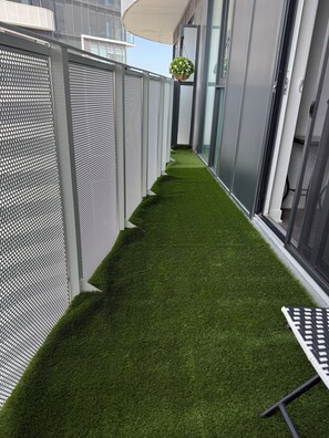 A narrow corridor with artificial grass, metal mesh walls, and a hanging plant.