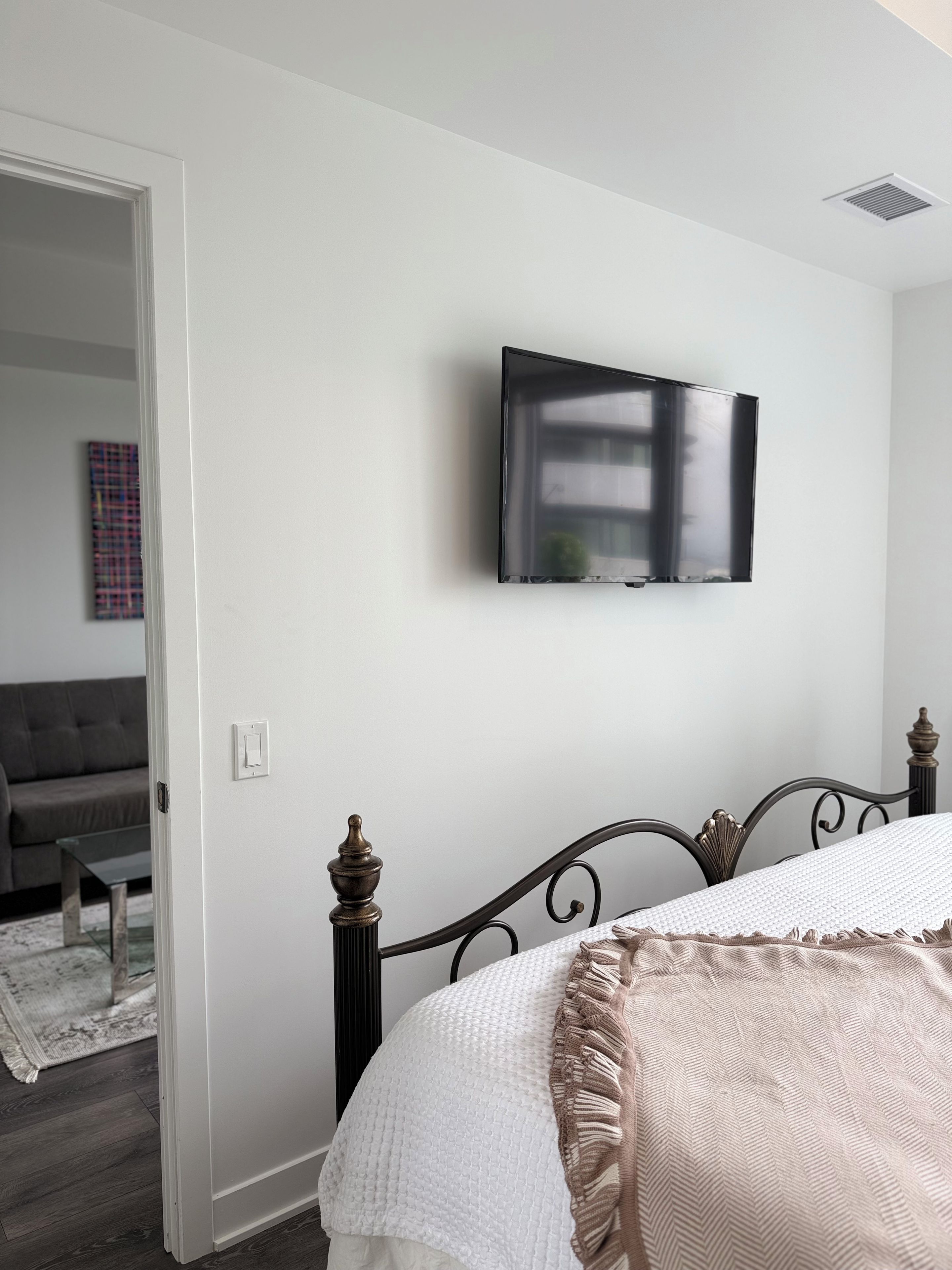 Une chambre à coucher avec un lit, un téléviseur fixé au mur et une porte donnant sur une autre pièce.