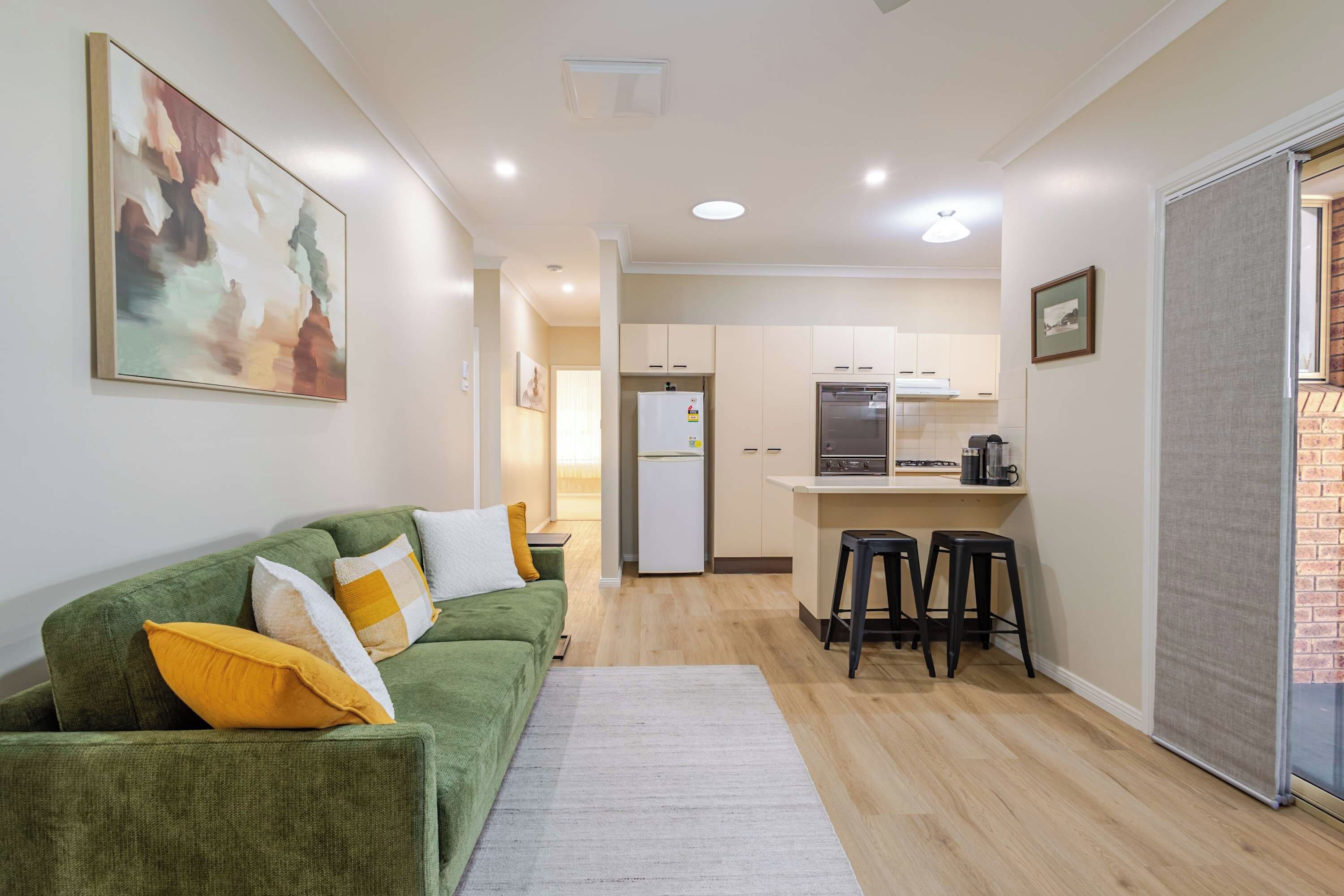 A compact living space with a green sofa, a kitchen area, and a small dining table.