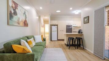 A compact living space with a green sofa, a kitchen area, and a small dining table.