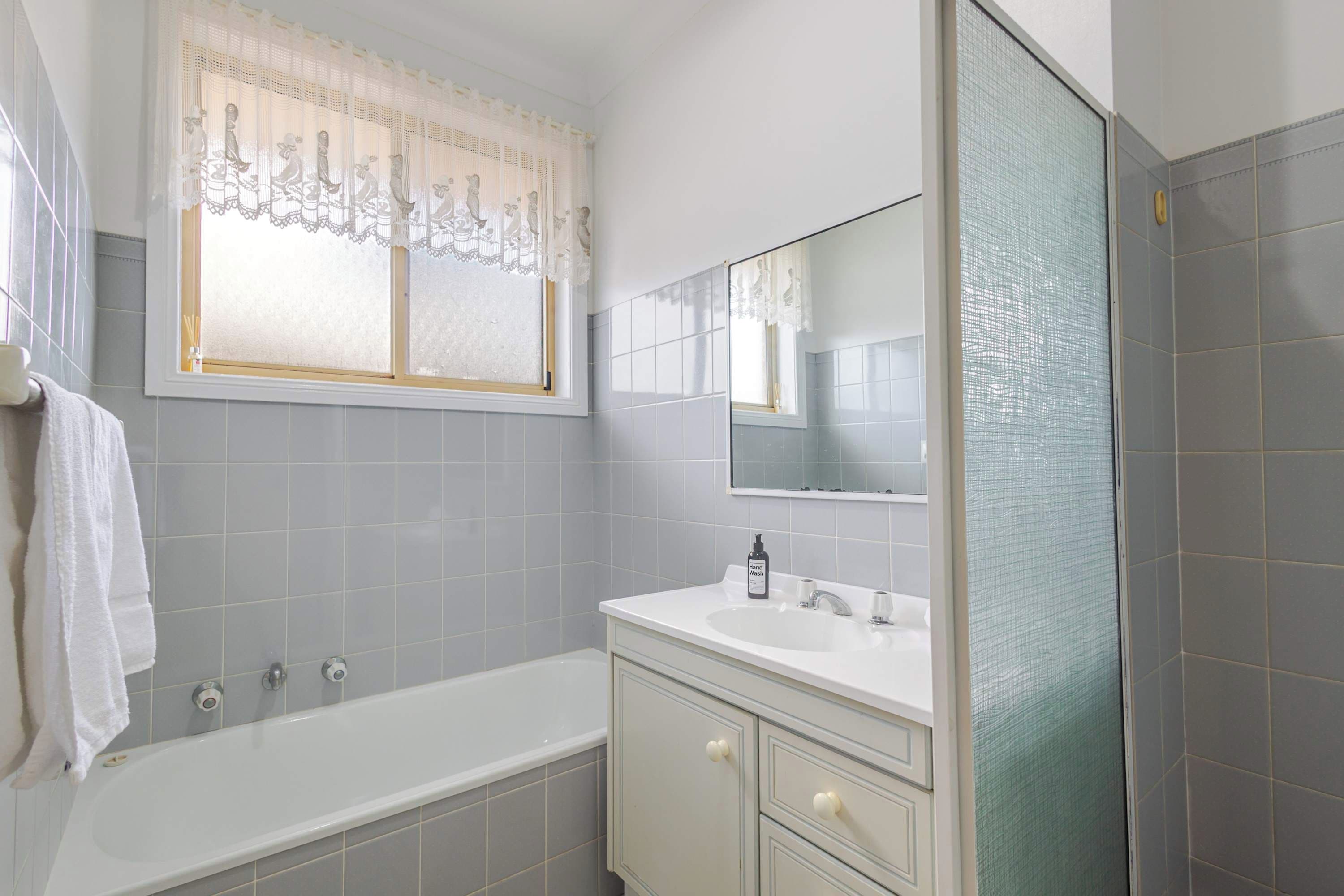 A bathroom with a bathtub, a sink with a mirror, and a window with lace curtains.
