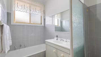 A bathroom with a bathtub, a sink with a mirror, and a window with lace curtains.