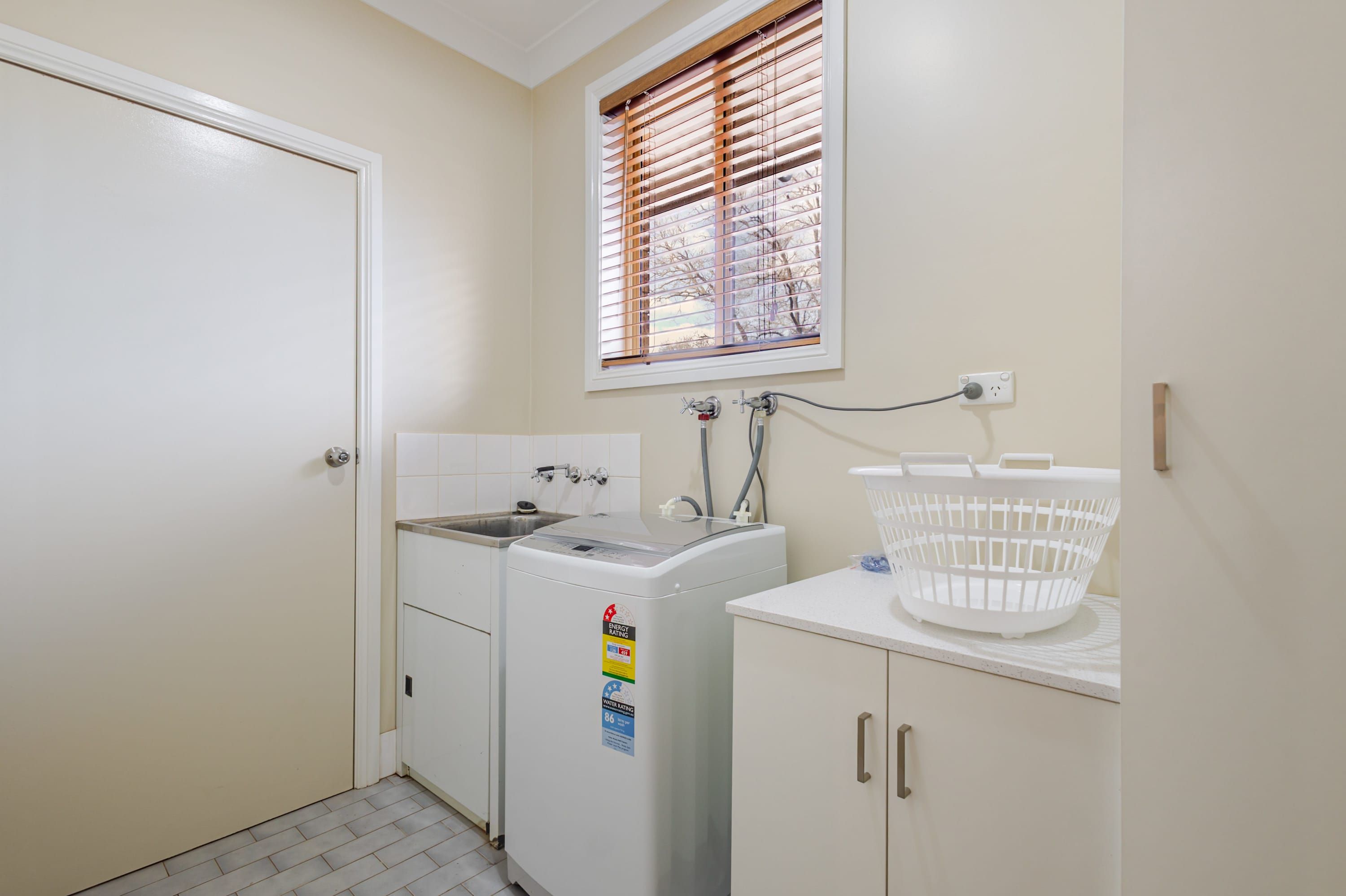 A laundry room with a washing machine, a sink, and a window with blinds.