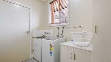 A laundry room with a washing machine, a sink, and a window with blinds.
