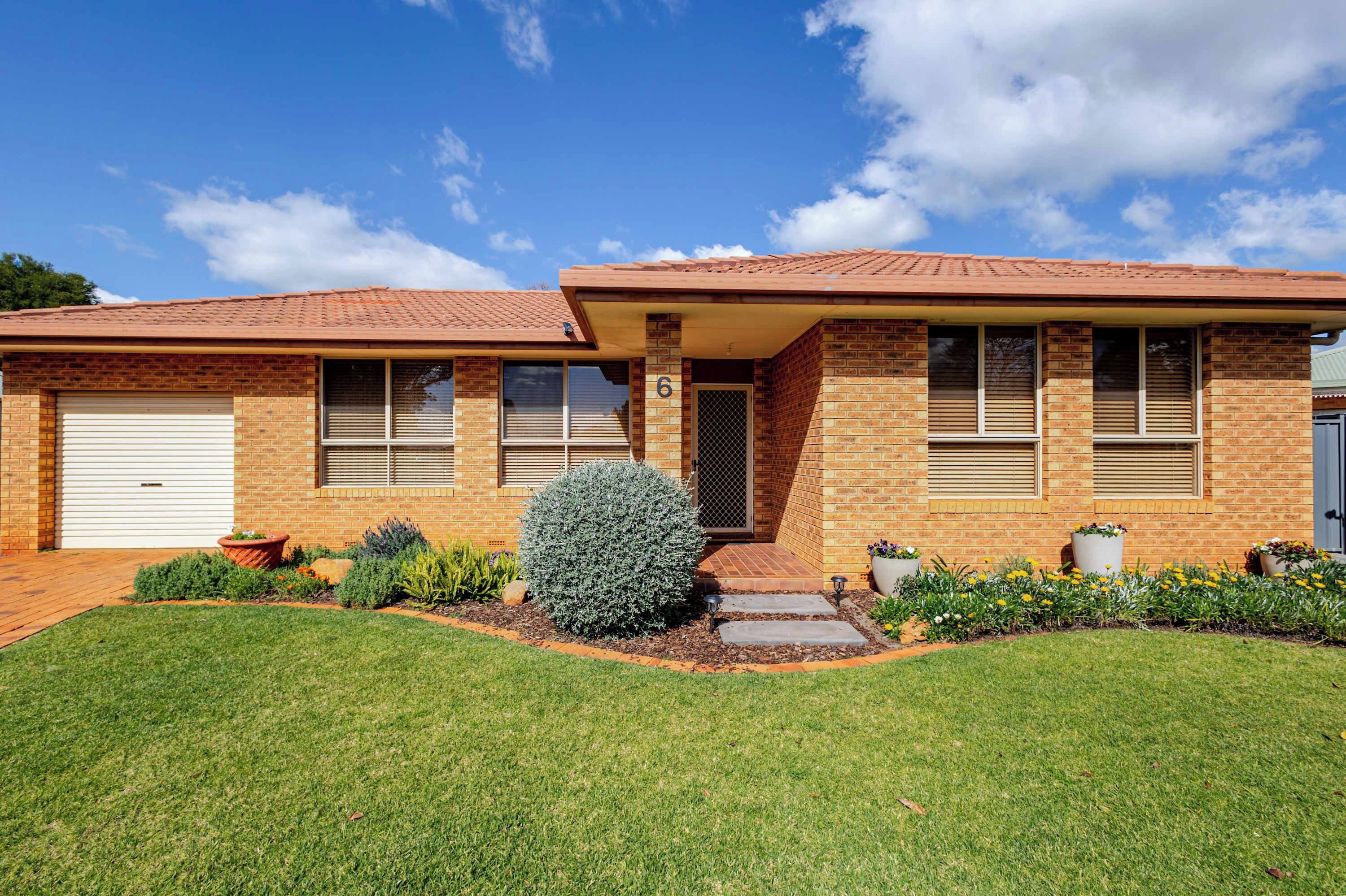 A two-story house with a brick facade, a garage, and a well-maintained front yard with a lawn and potted plants.