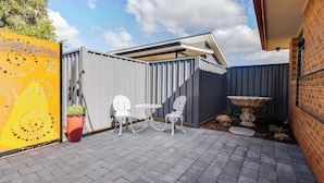 A patio area with two white chairs and a table, a potted plant, and a decorative stone feature. - House of Tudor II, Dubbo (Dubbo)