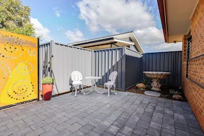 A patio area with two white chairs and a table, a potted plant, and a decorative stone feature. - House of Tudor II, Dubbo (Dubbo)