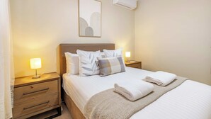 A hotel room with a bed, two bedside tables, a lamp, a wall-mounted air conditioner, and a framed picture. - House of Tudor II, Dubbo (Dubbo)