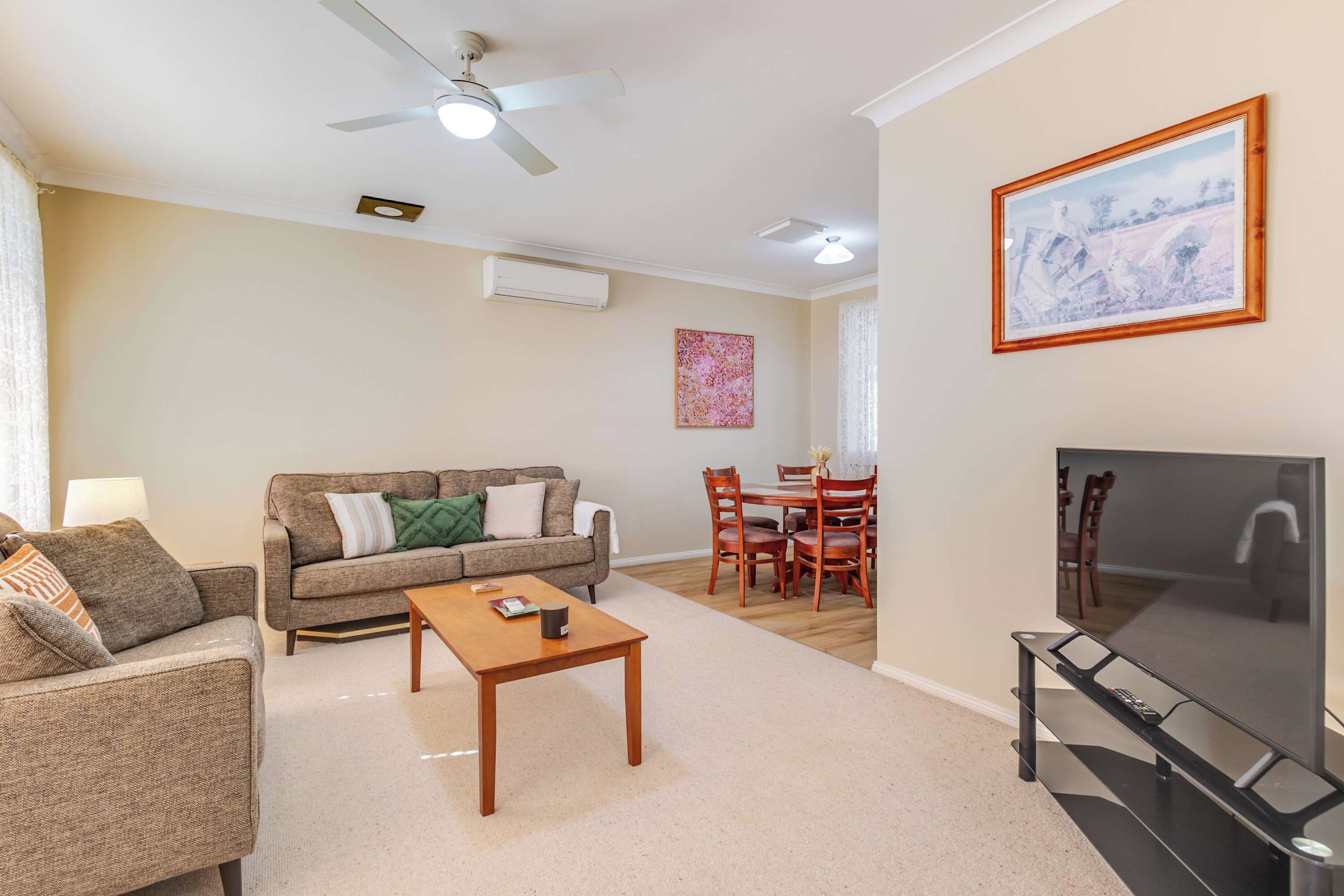A living room with a sofa, coffee table, TV, and a dining area with chairs and a table.