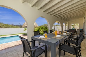 An outdoor dining area with a pool, covered seating, and a view of the landscape. - 3BD Villa Luma near Palm Beach and Ritz - Pool/BBQ (Noord)