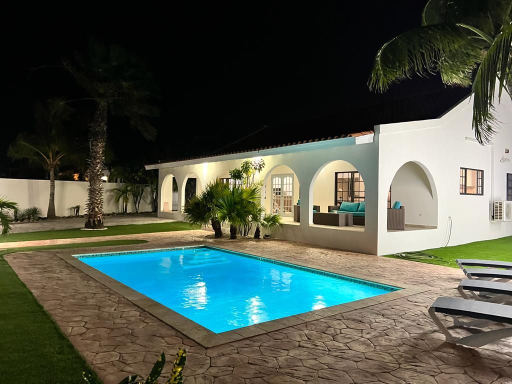 Ein modernes Haus mit Swimmingpool, Sitzgelegenheiten im Freien und Palmen.