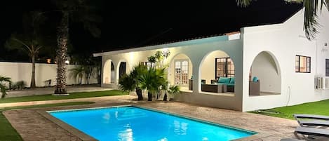 Ein modernes Haus mit Swimmingpool, Sitzgelegenheiten im Freien und Palmen.