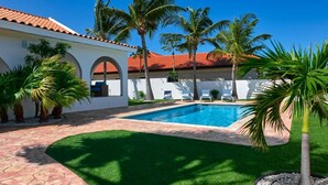 A swimming pool surrounded by palm trees and a white building with a red-tiled roof. - Renovated 3BR Home Private PoolClose 2 BeachBBQ (Noord)