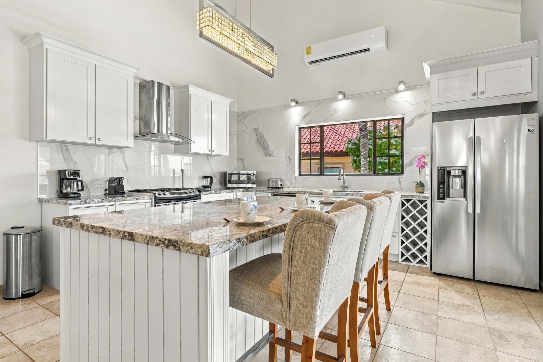 A modern kitchen with white cabinetry, a stainless steel refrigerator, and a large island with bar stools.