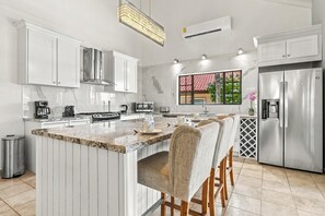 Une cuisine moderne avec des meubles blancs, un réfrigérateur en acier inoxydable et un grand îlot central doté de tabourets de bar.