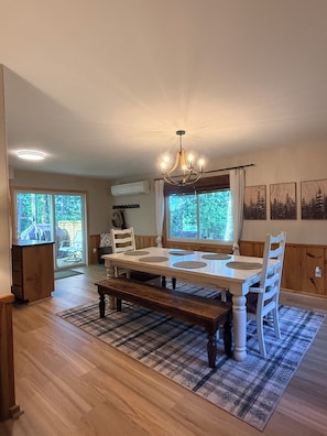 A dining area with a wooden table, white chairs, a bench, and a chandelier.
