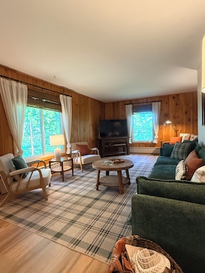 A cozy living room with wooden walls, a plaid rug, a green sofa, a wooden coffee table, and a television.