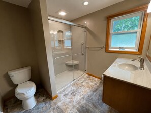 A bathroom with a glass-enclosed shower, a toilet, and a sink with a window above it.