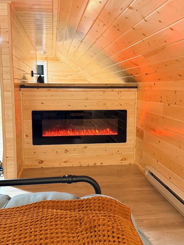 A wooden interior with a fireplace, a bed, and a blanket.