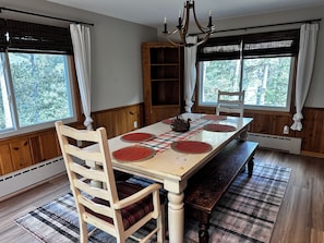 A dining room with a wooden table, chairs, a chandelier, and large windows with curtains.