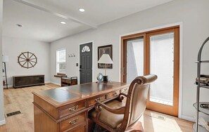 A spacious room with a wooden desk, leather chair, and a large window with blinds.