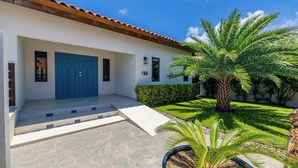 Un edificio con una porta blu, un ingresso piastrellato e un giardino curato con palme.
