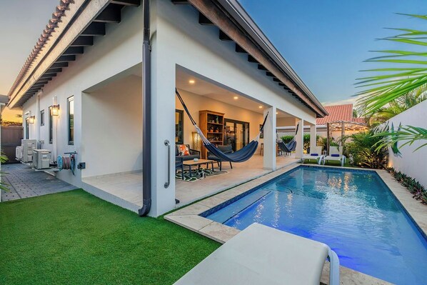 Een modern huis met een zwembad, terras en hangmat.