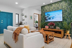 Een woonkamer met een bank, salontafel en een televisie die aan een muur met een tropisch bladpatroon is bevestigd.