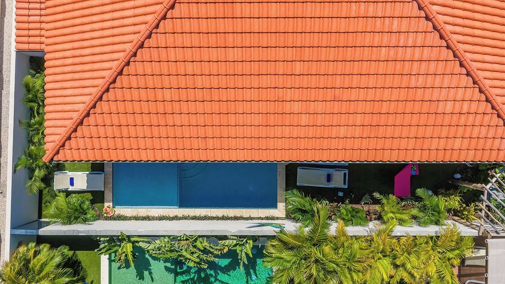 A building with a red-tiled roof, a blue door, and a small pool area with tropical plants.