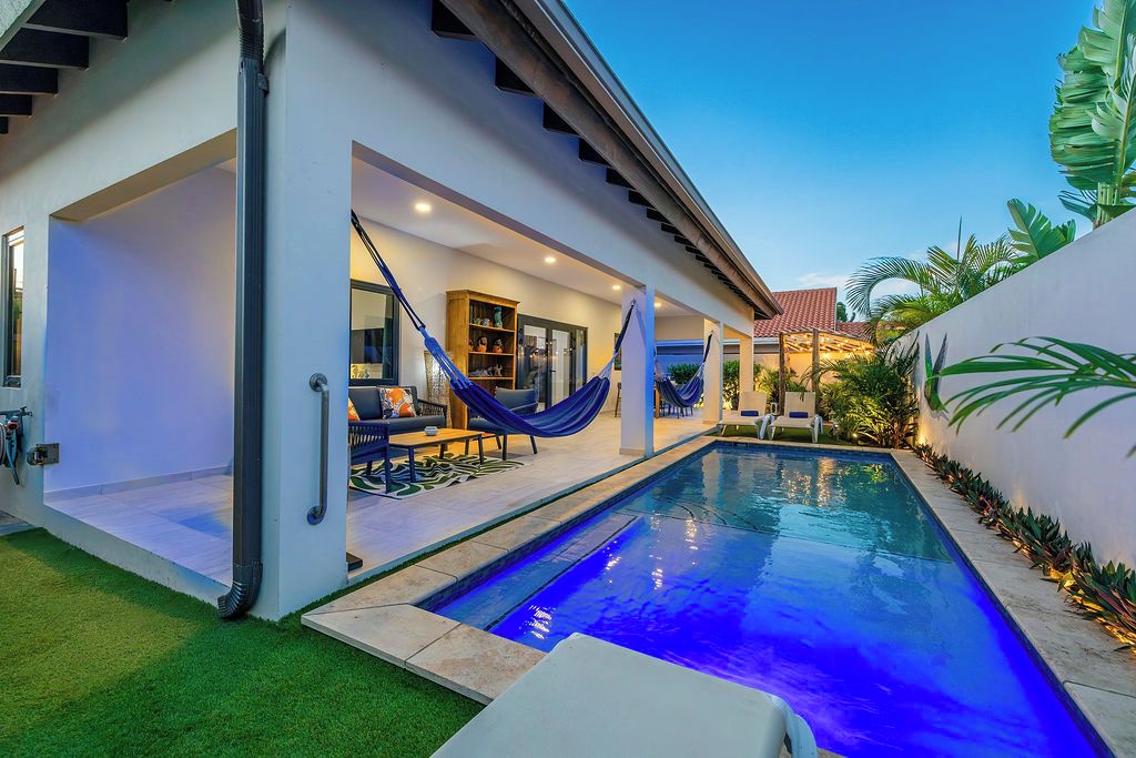 A modern house with a swimming pool, outdoor seating, and a covered patio area.
