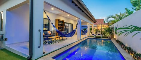 A modern house with a swimming pool, outdoor seating, and a covered patio area.