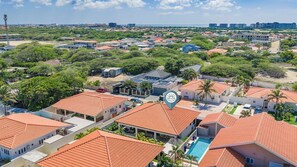 A residential area with multiple houses, a swimming pool, and a large building with a distinctive logo. - Villa Prikichi II ~ Close to Beach w/ Private Pool (Noord)