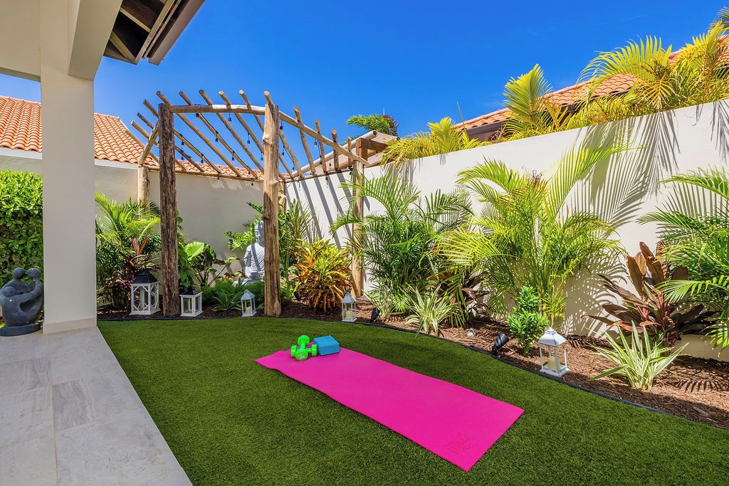 A patio area with artificial grass, a wooden pergola, and various plants.