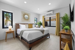 Een moderne slaapkamer met een groot bed, nachtkastjes, een aan de muur bevestigde televisie en een raam met gordijnen.